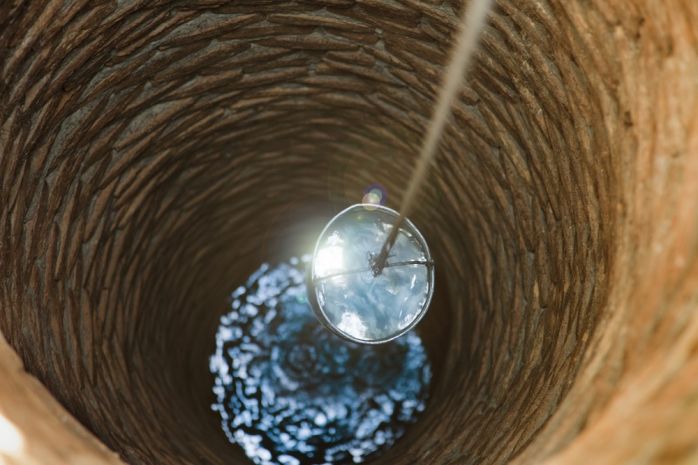Wasser wird mit einem Eimer aus dem Brunnen geholt